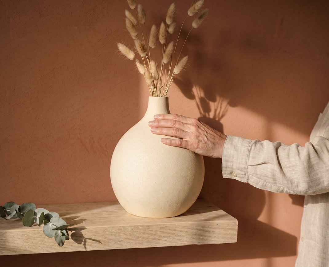 Hand resting on a sculptural vessel filled with dried grasses